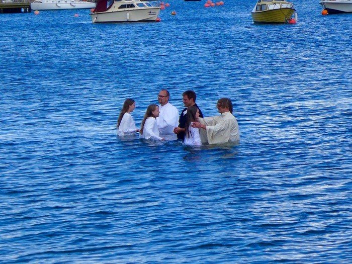 Taufzeremonie im Freien in blauem Wasser mit mehreren Teilnehmern.