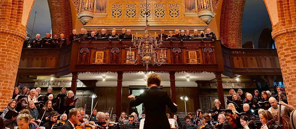 Chor und Orchester treten in einer Kirche mit großer Orgel auf.